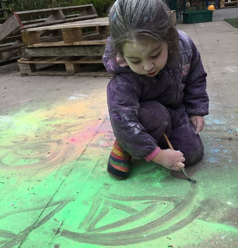 A young girl drawing on the floor outside